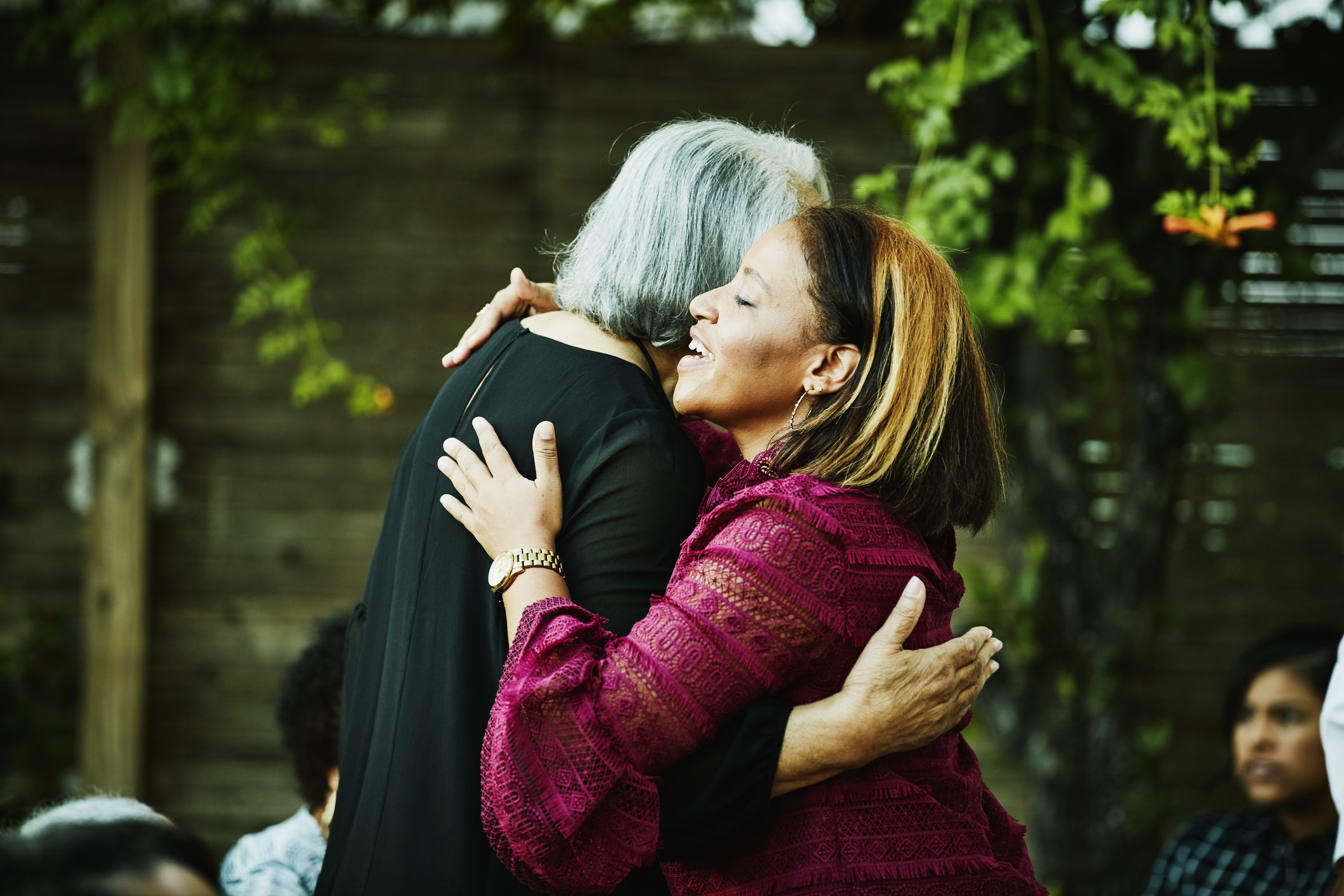 Mature niece hugging senior aunt before outdoor dinner party with family